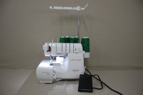 A white Baby Lock Accolade serger with green thread spools and a foot pedal.