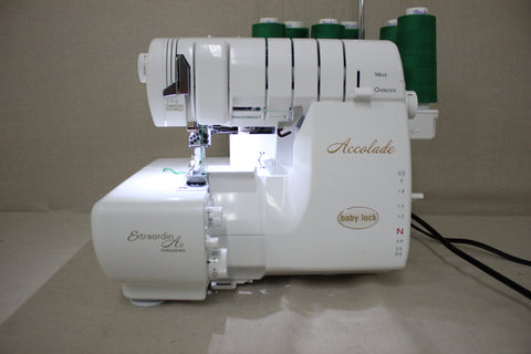 A white Baby Lock Accolade serger with green thread spools on top.