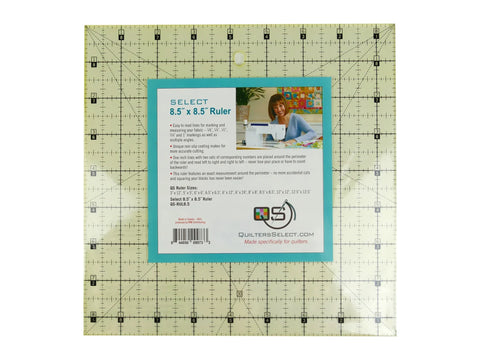 A square, clear quilting ruler with black grid lines and a teal label featuring a woman sewing.