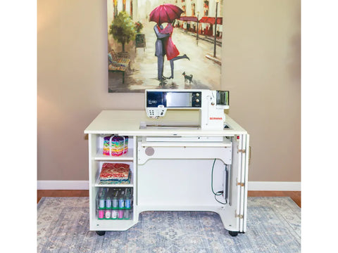 A white sewing cabinet with an electric lift sewing machine, fabric, and thread on shelves.