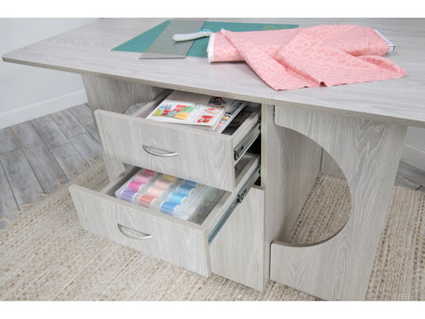 A light wood Koala Cutting Table with two open drawers, fabric, and cutting tools on top.