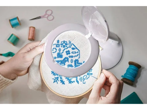 A person cross-stitching with a white, rechargeable magnifying lamp illuminating their work.