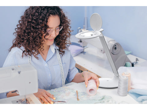 Daylight Halo Go Rechargeable Magnifier illuminating a woman sewing intricate fabric.
