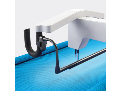 A white quilting machine arm with a black flexible lamp illuminates a blue quilted fabric.