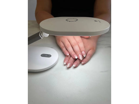 A white Foldi Go Rechargeable Table Lamp illuminates a person's hands with white swirl nail art.