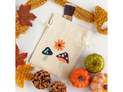 An embroidered drawstring bag with autumn leaves, pinecones, and decorative pumpkins.