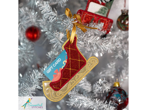 A red and gold sleigh-shaped gift card holder hangs on a white Christmas tree.