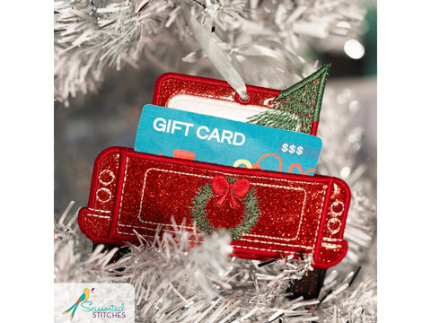 A red glittery truck ornament with a gift card and a small Christmas tree.