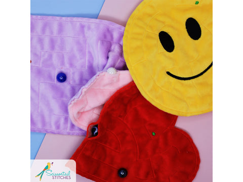 Three plush, colorful in-the-hoop mazes are shown, one purple, one red, and one yellow.