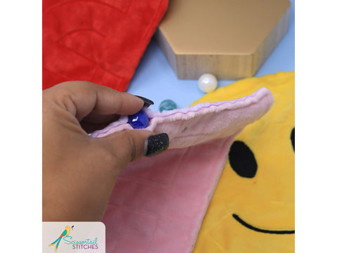 A hand holds a pink plush maze with a blue marble, next to a yellow smiley face.