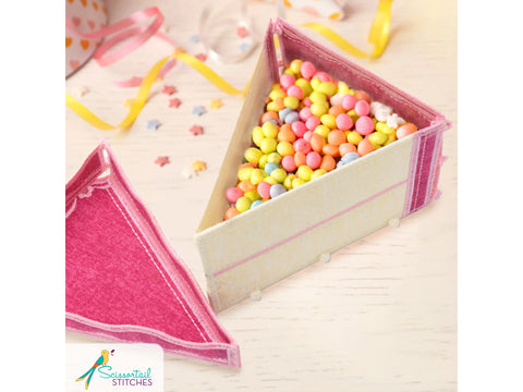 A freestanding fabric cake box filled with colorful candies, with a pink lid beside it.