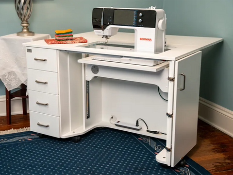 White sewing cabinet with four drawers, an electric lift, and a Bernina sewing machine.