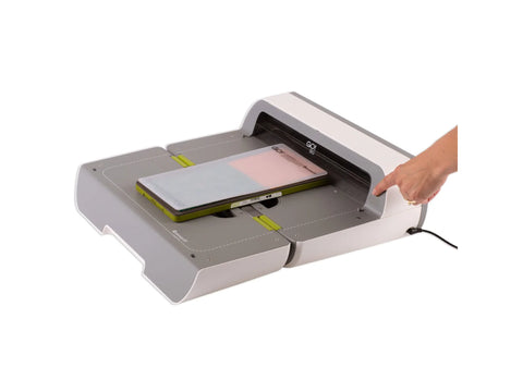 A person's hand presses a button on the AccuQuilt GO! Big Electric Fabric Cutter.