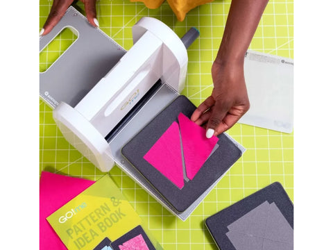 A person uses the AccuQuilt GO! Me fabric cutter to cut pink fabric.