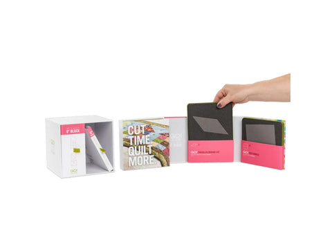 A hand places a dark gray parallelogram die into a white box with pink accents.