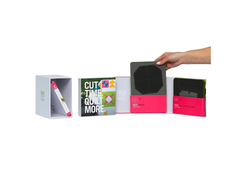 A hand holds a dark gray cutting die above a set of quilting tools and guides.