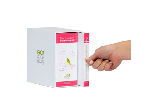 A hand pulls a white box with pink and green accents from a larger white box.