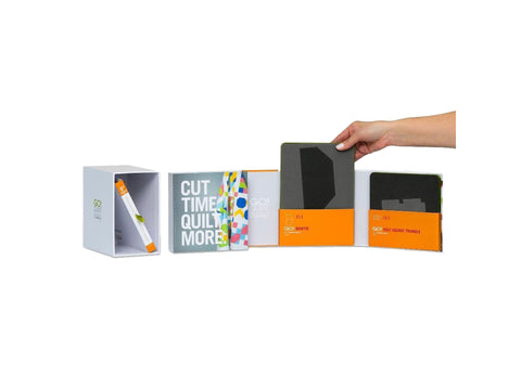 A hand places a dark gray fabric cutting die into an open white box with other dies and books.