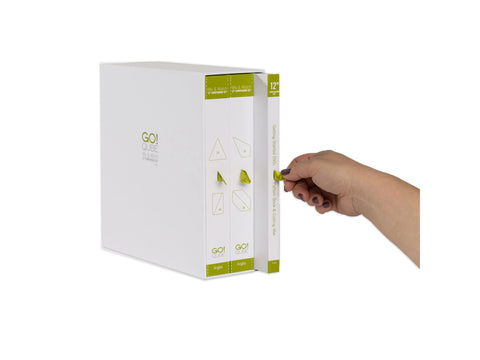 A hand pulls out a green-labeled book from a white box set of AccuQuilt Qube Companion Angles.