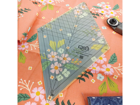 A clear Quilters Select 60 Degree Diamond ruler on floral fabric with a rotary cutter.