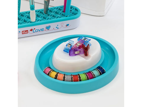 Prym Love magnetic pin cushion with a bobbin ring holding colorful bobbins and clips.