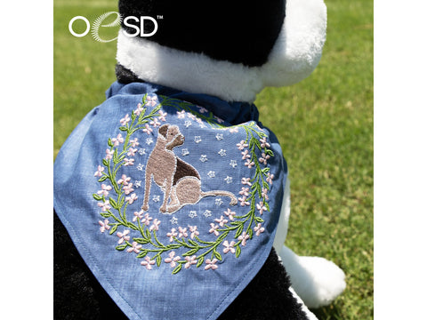 A plush dog wears a blue bandana embroidered with a dog surrounded by a floral wreath.