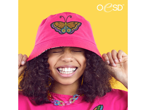 A smiling person wearing a pink bucket hat with a colorful butterfly embroidery.