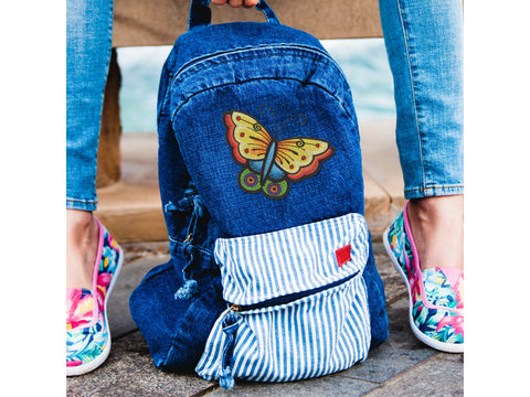 A denim backpack with a colorful butterfly embroidery and a striped front pocket.