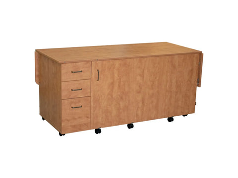 Light brown sewing cabinet with three drawers and drop leaves on wheels.