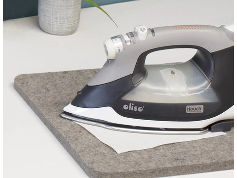 A gray and white Oliso iron rests on a gray wool pressing mat.