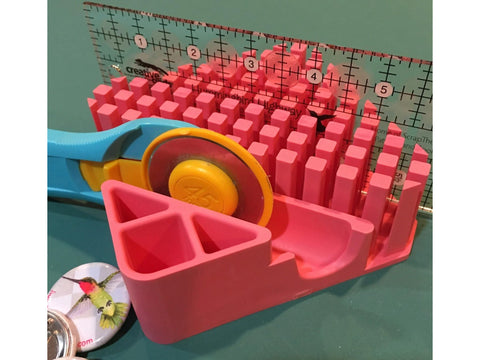 A flamingo pink organizer holds a blue and yellow rotary cutter and a clear ruler.
