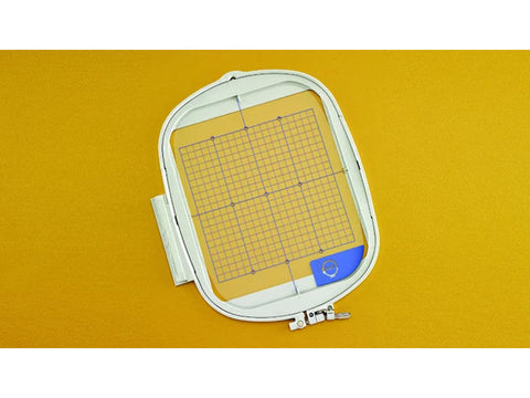 An 8" x 8" embroidery hoop with a grid insert rests on a yellow surface.
