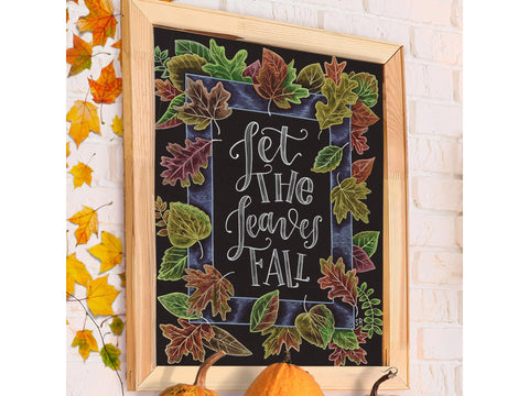 A framed chalkboard sign with "Let the Leaves Fall" in white script, surrounded by colorful autumn leaves.