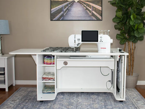 A white sewing and embroidery cabinet with a sewing machine, open shelves, and expandable surfaces.