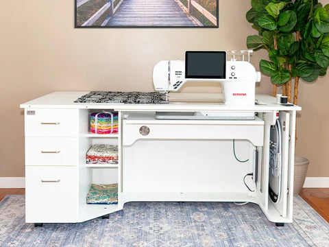 A white sewing and embroidery cabinet with a sewing machine, fabric, and thread.