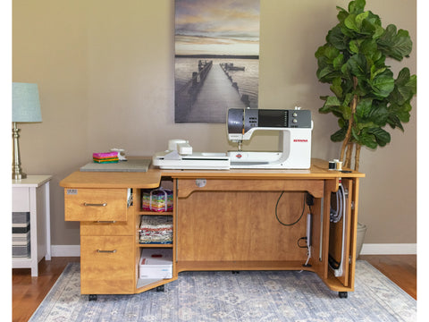 A light wood sewing and embroidery cabinet with a sewing machine on top.