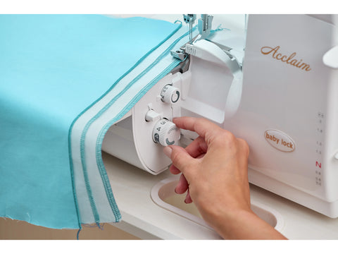 A person adjusts a white Baby Lock Acclaim serger with blue fabric.
