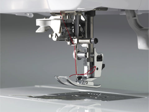 A close-up of a sewing machine's needle and presser foot with red thread.