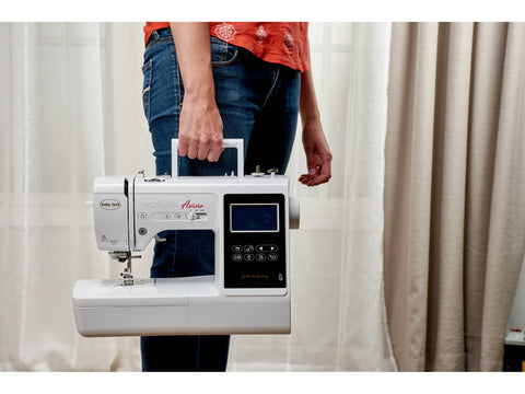 A person holds a white Baby Lock Aurora sewing and embroidery machine.