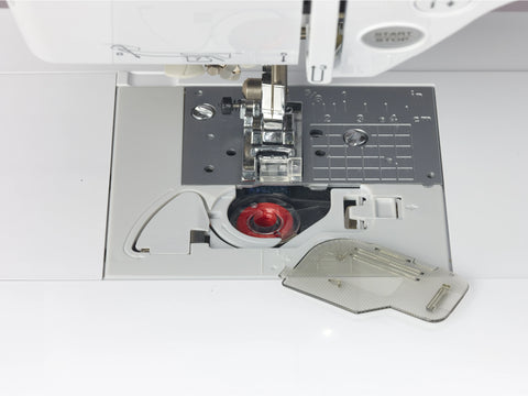 A close-up of a sewing machine's bobbin area with a red bobbin and open cover.