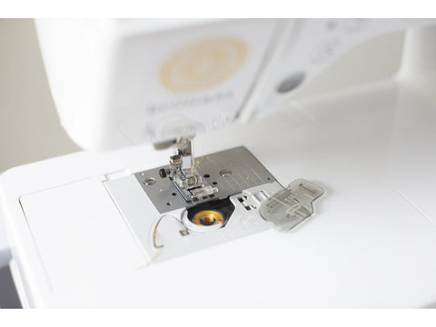 A close-up of a white Baby Lock Brilliant sewing machine with the bobbin area open.
