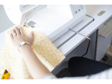 A person sews yellow patterned fabric on a white Baby Lock Brilliant sewing machine.