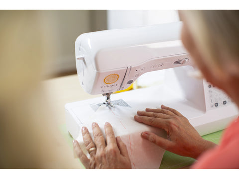 A person's hands guide white fabric through a Baby Lock Brilliant sewing machine.
