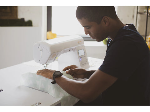 A man sews light green fabric with white triangles on a white Baby Lock Brilliant sewing machine.