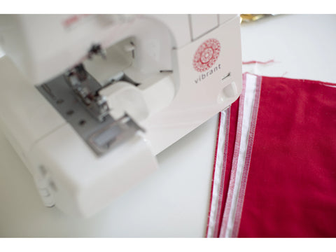 A white Baby Lock Vibrant serger with red fabric and white stitching.