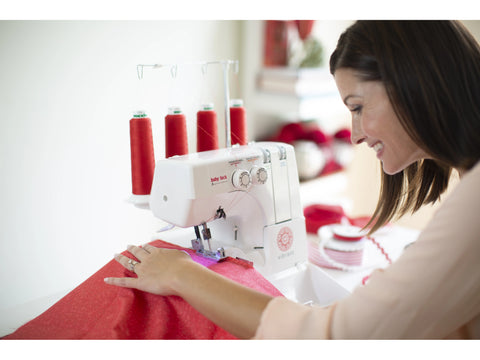 A woman uses a white Baby Lock Vibrant serger with red thread to sew red fabric.