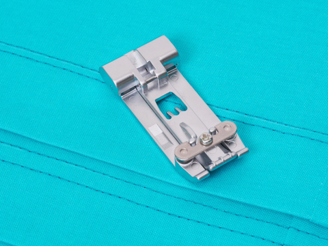 A silver Baby Lock compensating serger foot rests on teal fabric with parallel stitching.