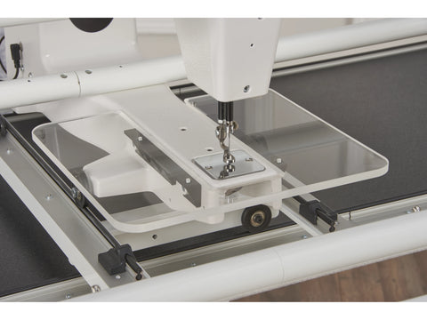 A close-up of a white long arm quilting machine with a clear acrylic extension table.