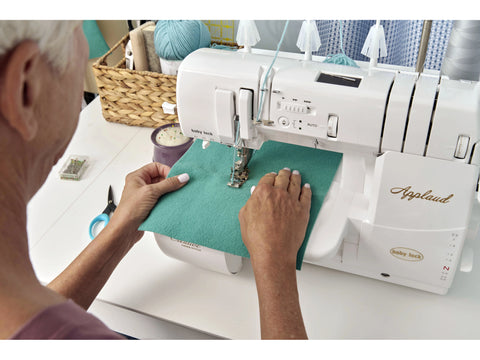 A person uses a white Baby Lock Applaud cover stitch machine to sew teal fabric.