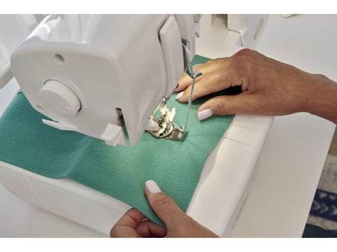 A person uses a white Baby Lock Applaud serger to sew green fabric.